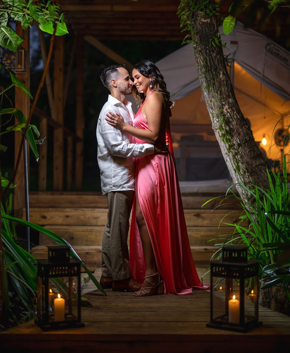 A couple shares an intimate evening moment on outdoor stairs illuminated by glowing lanterns and natural greenery.
