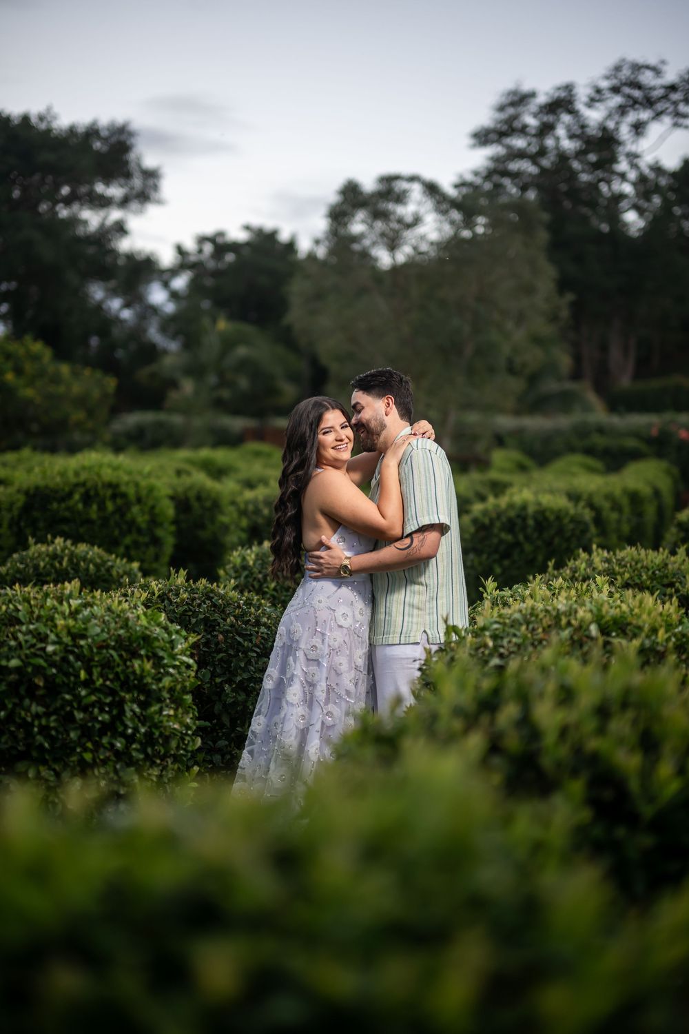 View of a couple embracing in an outdoor garden setting with lush greenery creating a romantic scene at dusk.
