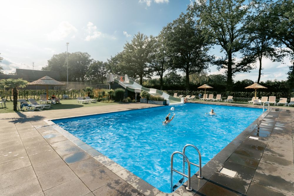 Panoramic view of a resort swimming pool surrounded by lounge chairs and trees.