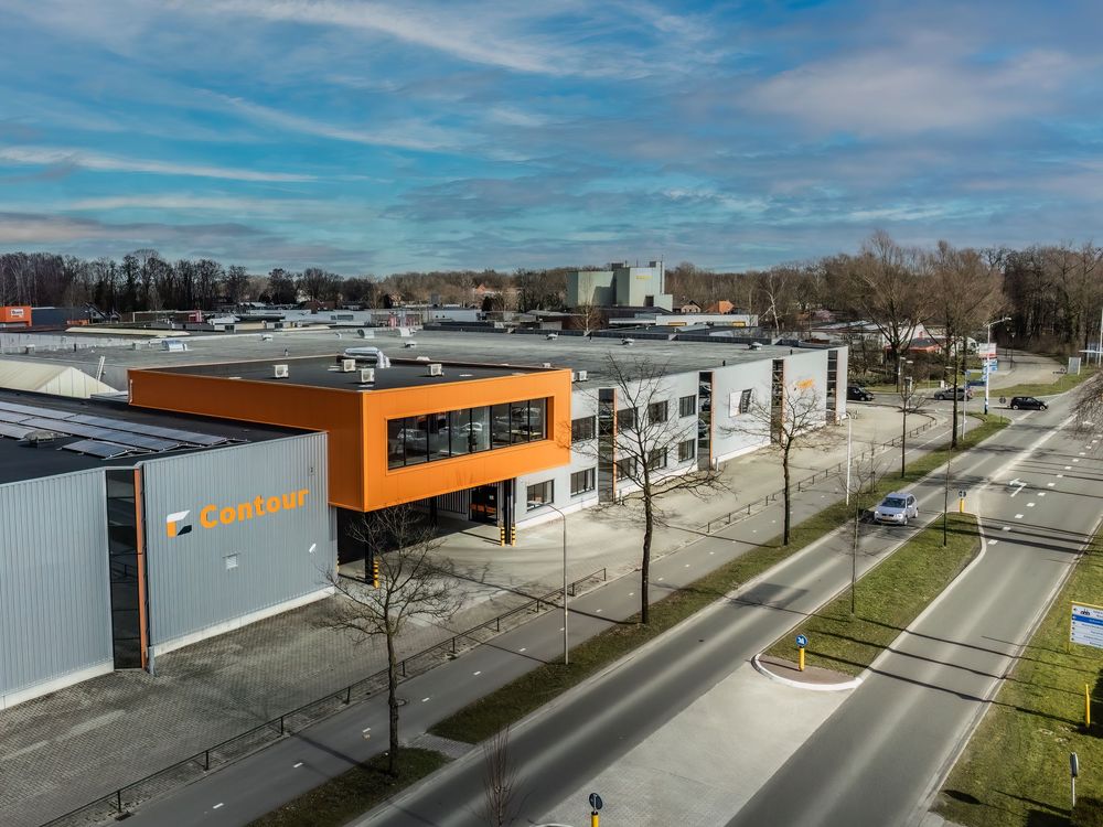 Aerial view of modern industrial park buildings with orange architectural accents under blue sky.