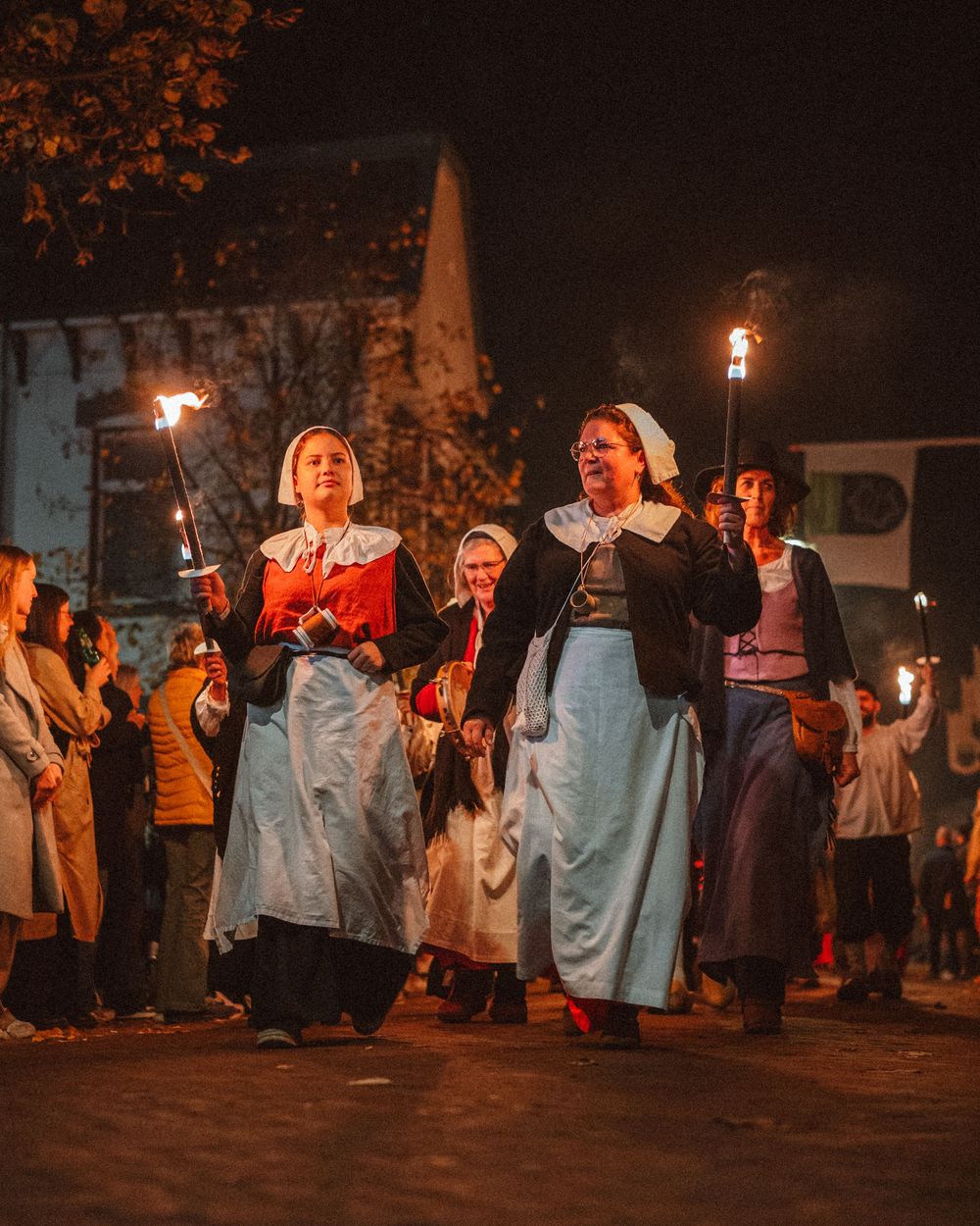 Group of people in historical costumes holding torches during a nighttime reenactment.
