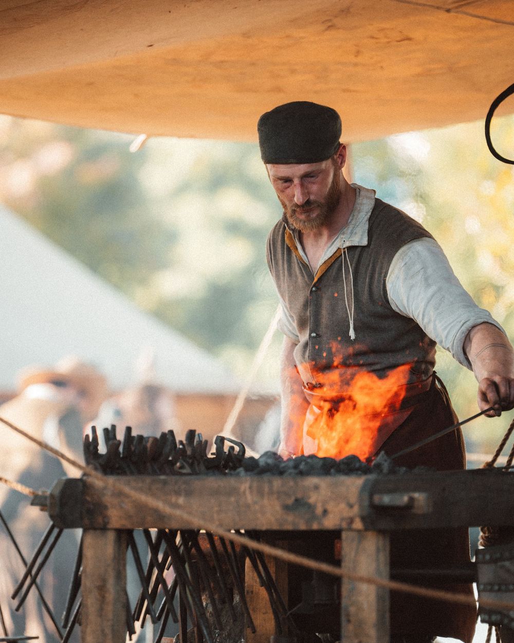 Blacksmith working with hot metal at a forge during a historical demonstration.