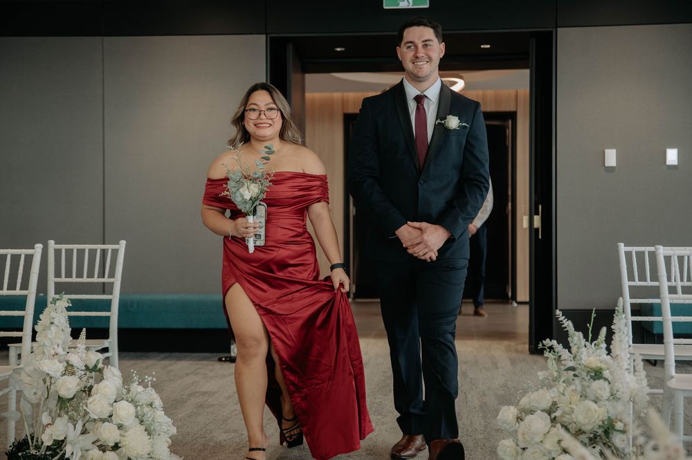 Wedding guests walk past elegant white floral arrangements and chairs during an indoor ceremony.