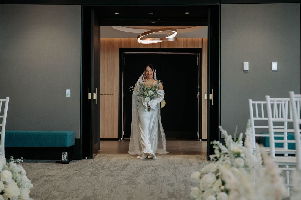 A formal wedding ceremony with white floral decorations at a modern venue entrance.