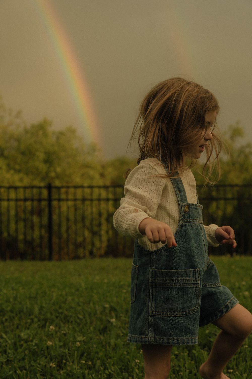 A series of images showing a person in denim overalls dancing in a field with a rainbow in the background.