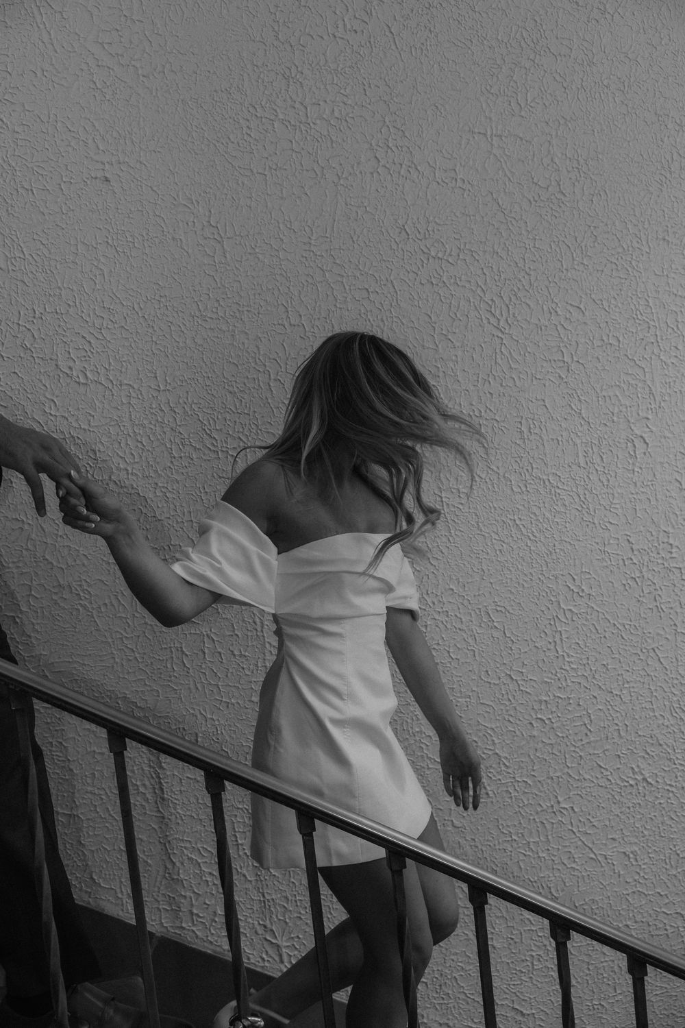 Black and white sequence shows figure in white dress descending staircase in artistic motion.