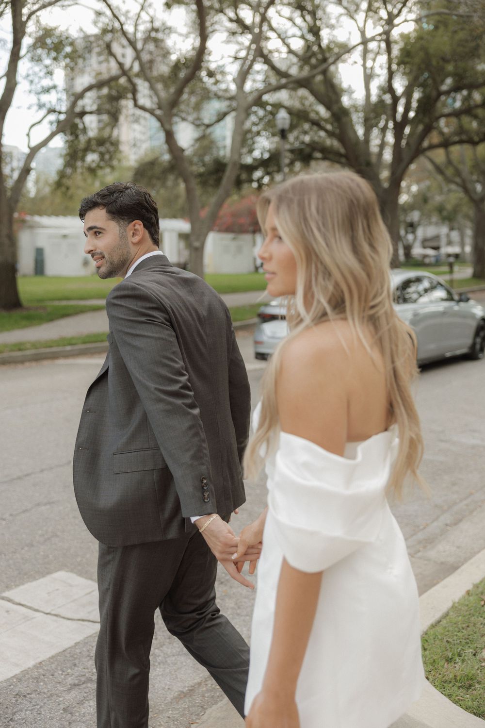 Wedding couple walking together outdoors with trees lining the street.