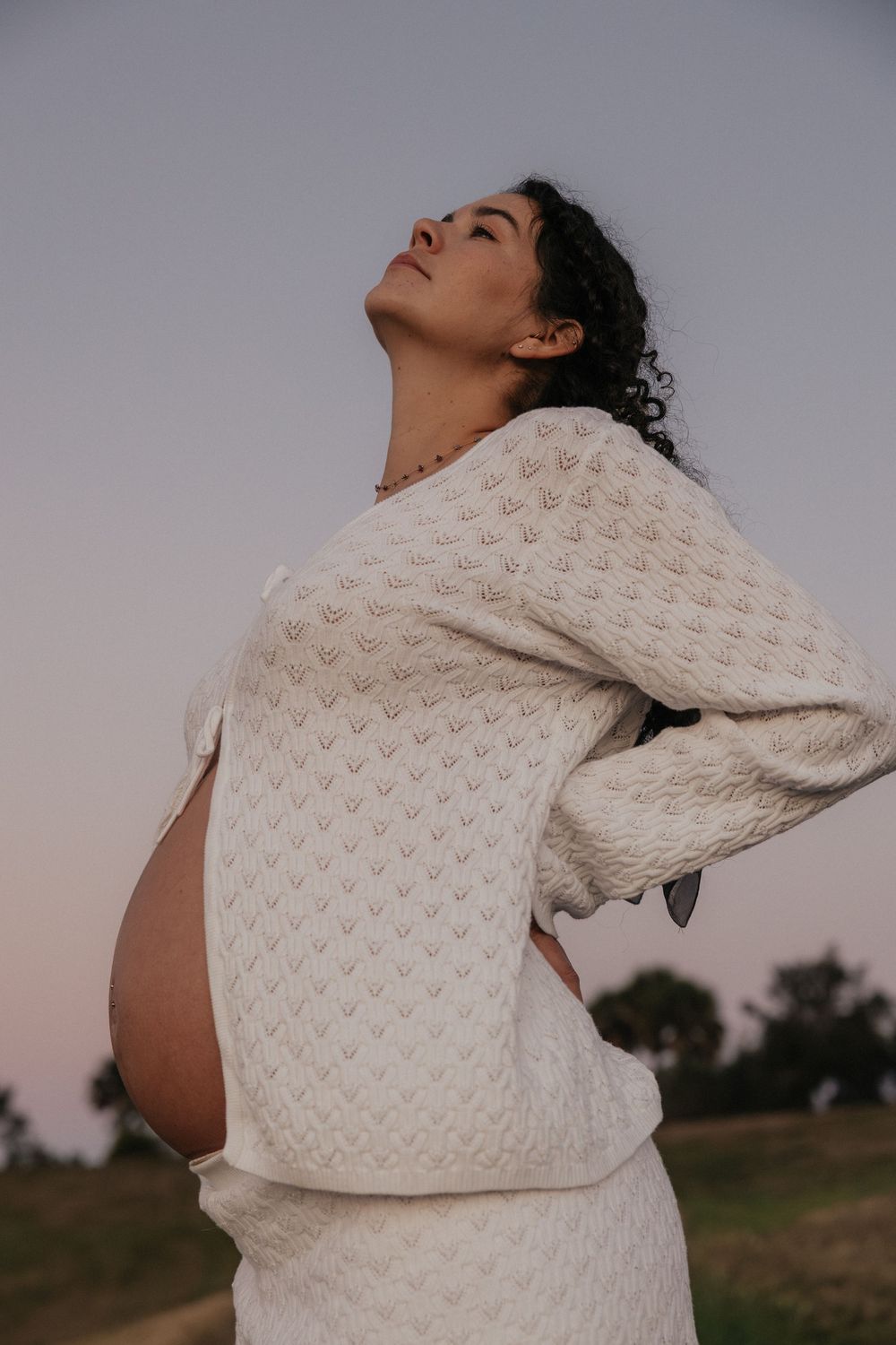 A series of artistic maternity photos showing a pregnant figure in a cream knit sweater against a dusky outdoor setting.