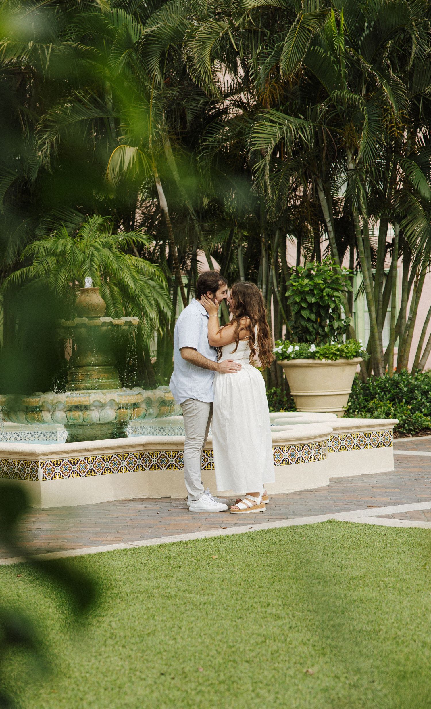 A romantic moment shared between two people sitting on a garden courtyard bench surrounded by lush tropical landscaping.