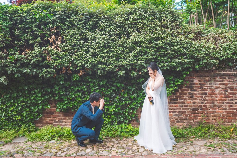 A romantic photo series of a couple in wedding attire posing together in front of an ivy-covered brick wall.