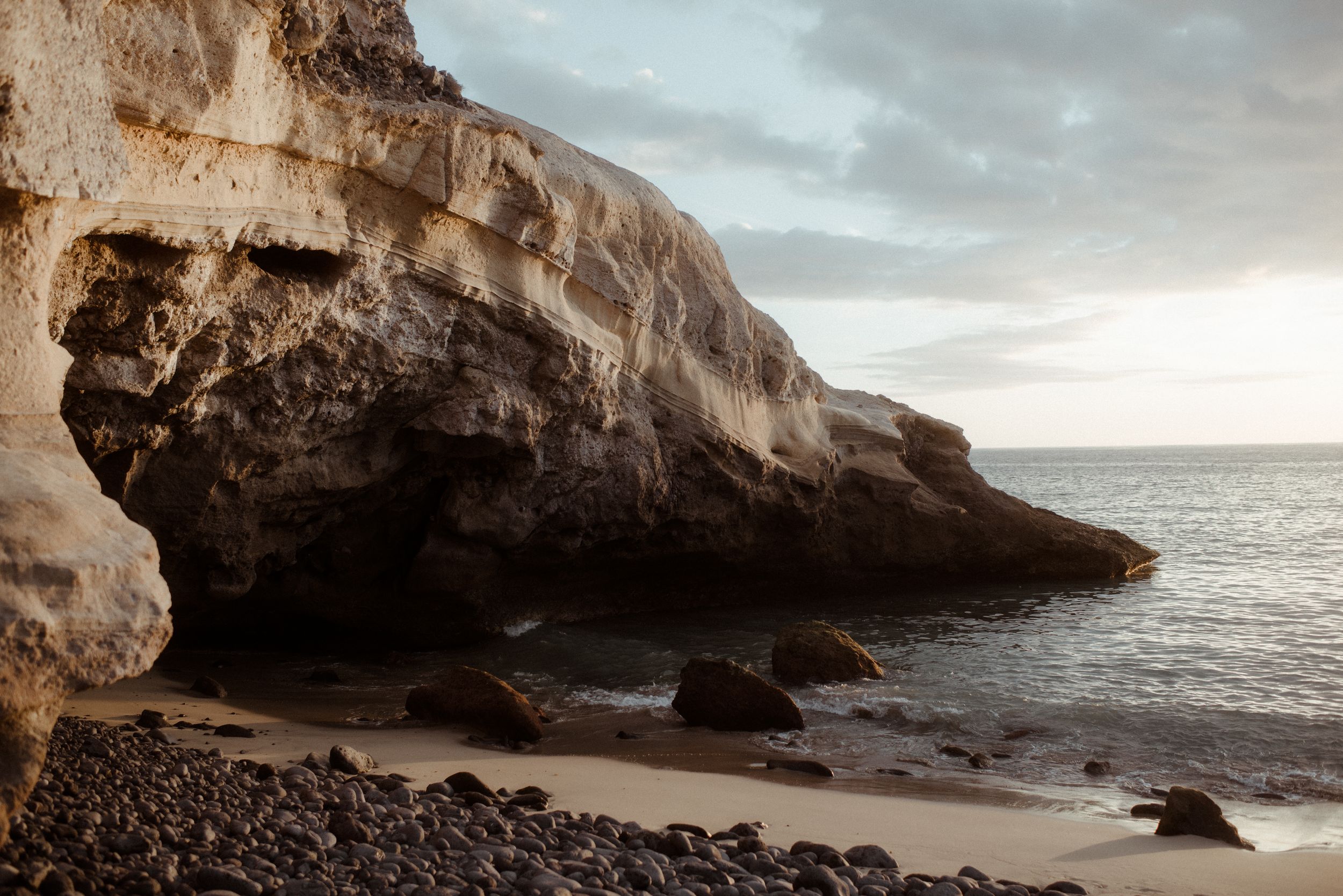 Rocky coastal caves and cliffs along a dramatic ocean shoreline during sunset create a moody seascape at Costa Adeje.