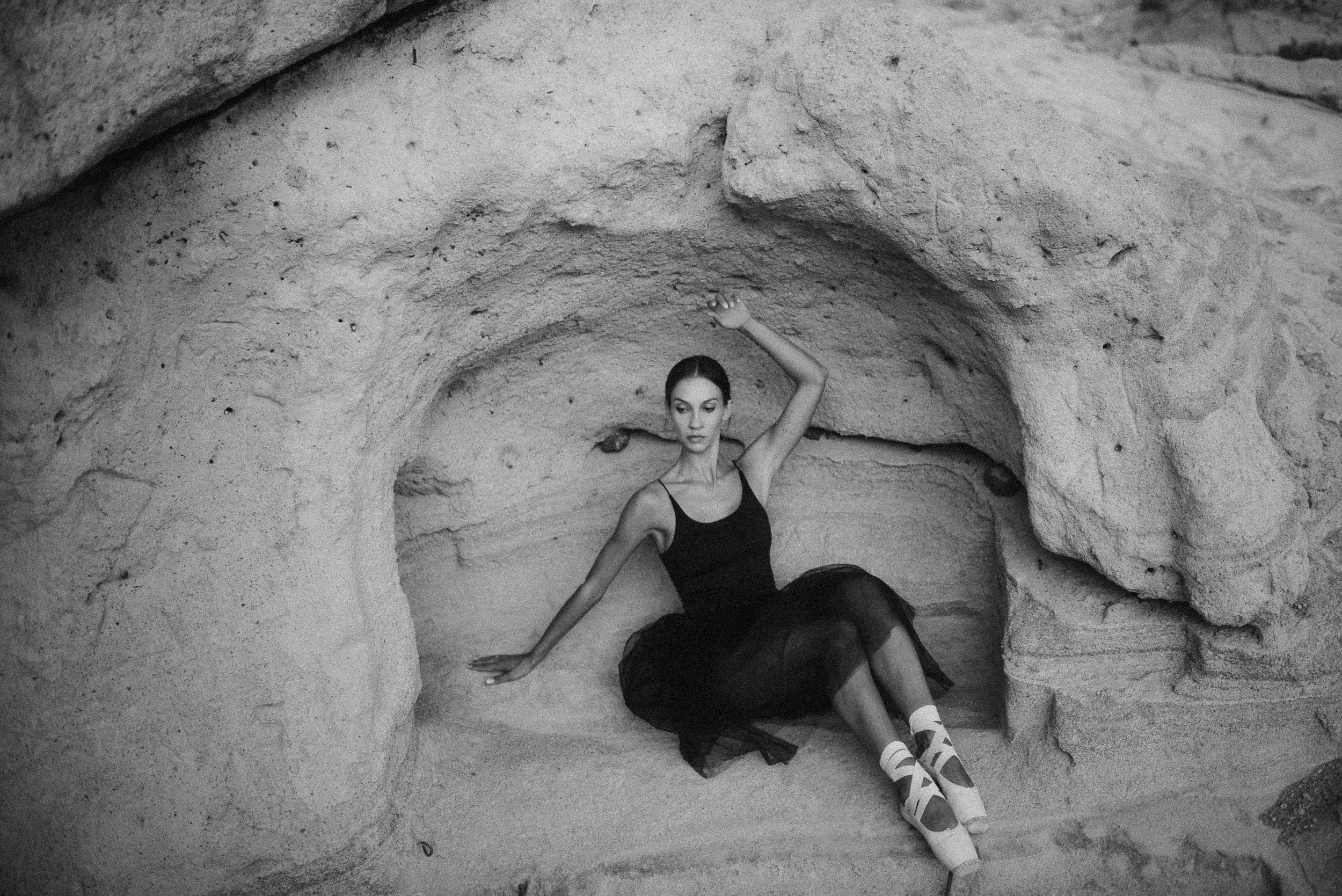 A ballerina sitting at natural rock formations and caves during an outdoor adventure in La Caleta de Adeje, Tenerife.