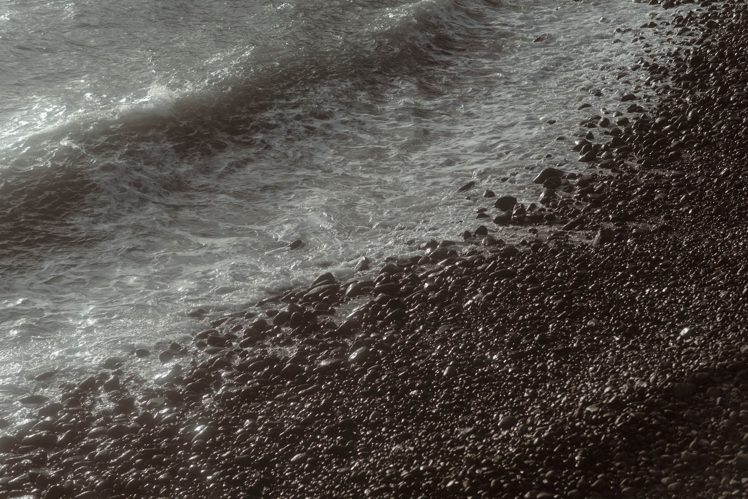 Aerial view of dark volcanic rocks and sand formations along a dramatic coastline with crashing ocean waves in La Caleta de Adeje, Tenerife.