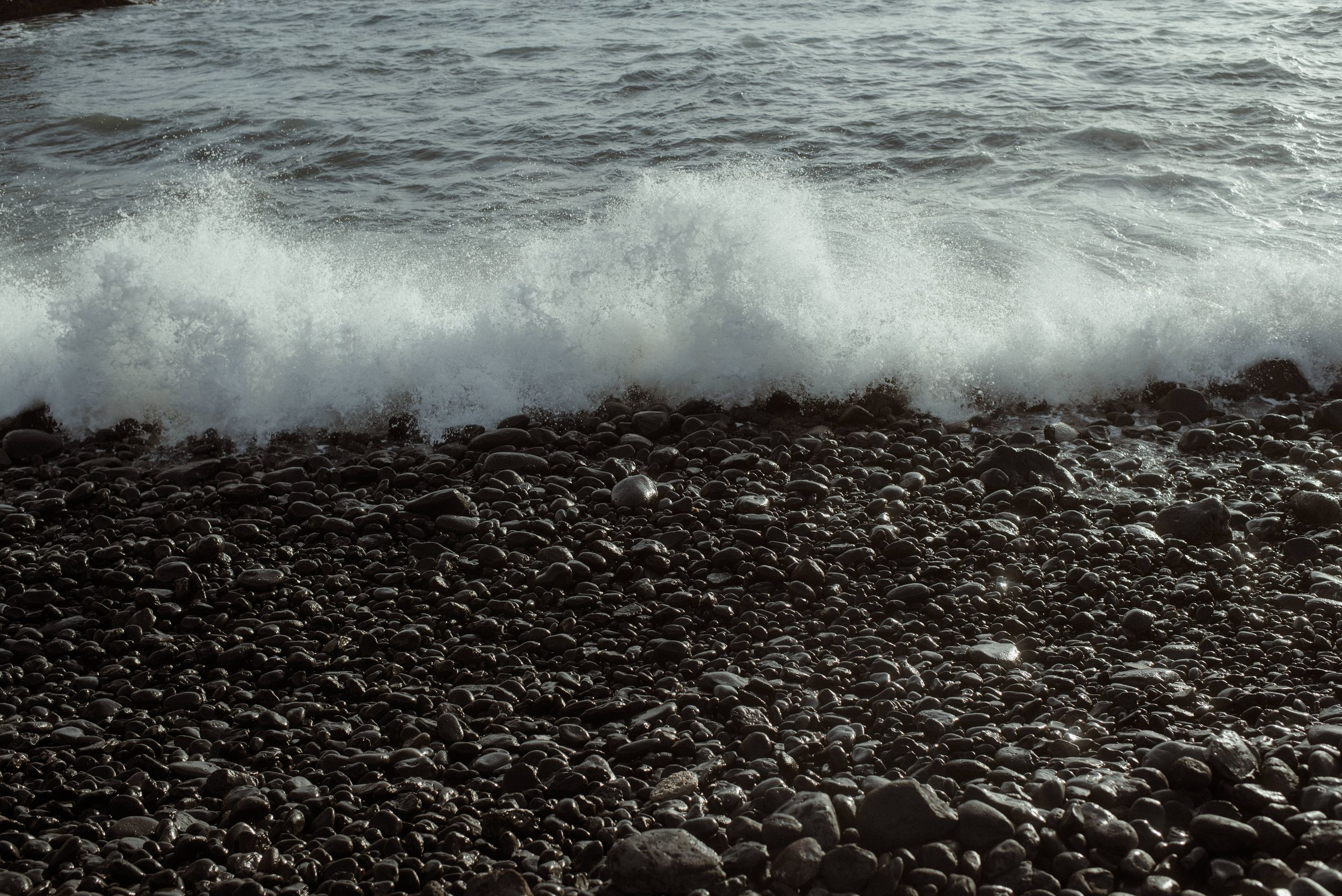 Waves from a rough ocean crash against a dark, rocky shoreline under dramatic stormy skies in La Caleta de Adeje, Tenerife.