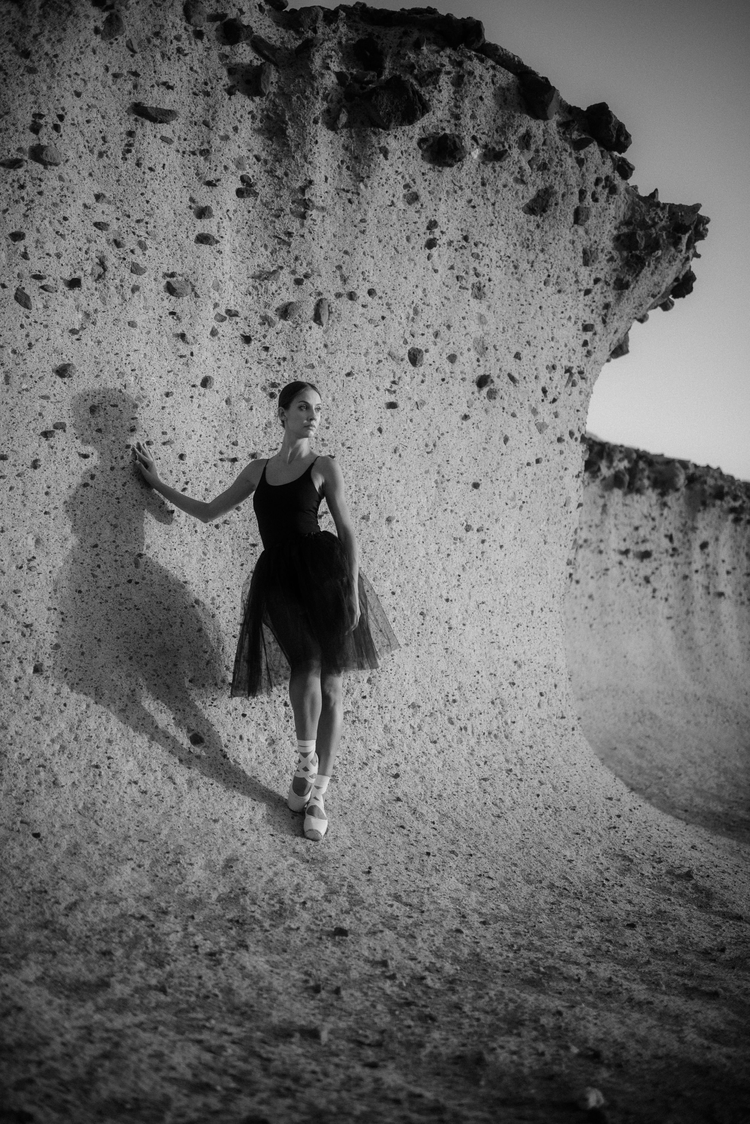 A ballerina in a black dress poses gracefully against a stark white limestone cliff face in black and white photography at Costa Adeje.