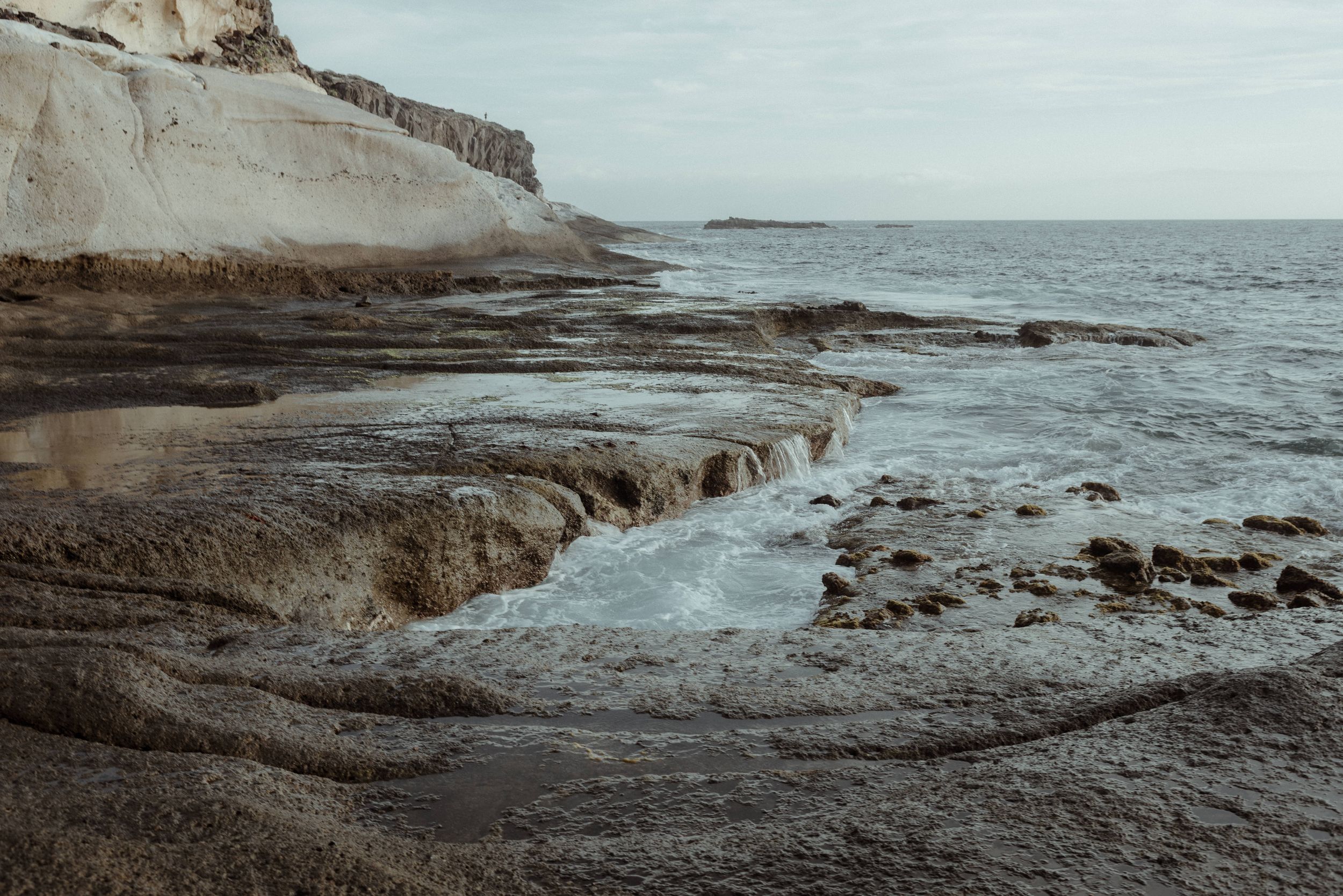 Rocky coastal landscape with waves crashing against weathered limestone cliffs at sunset in La Caleta de Adeje, Tenerife.