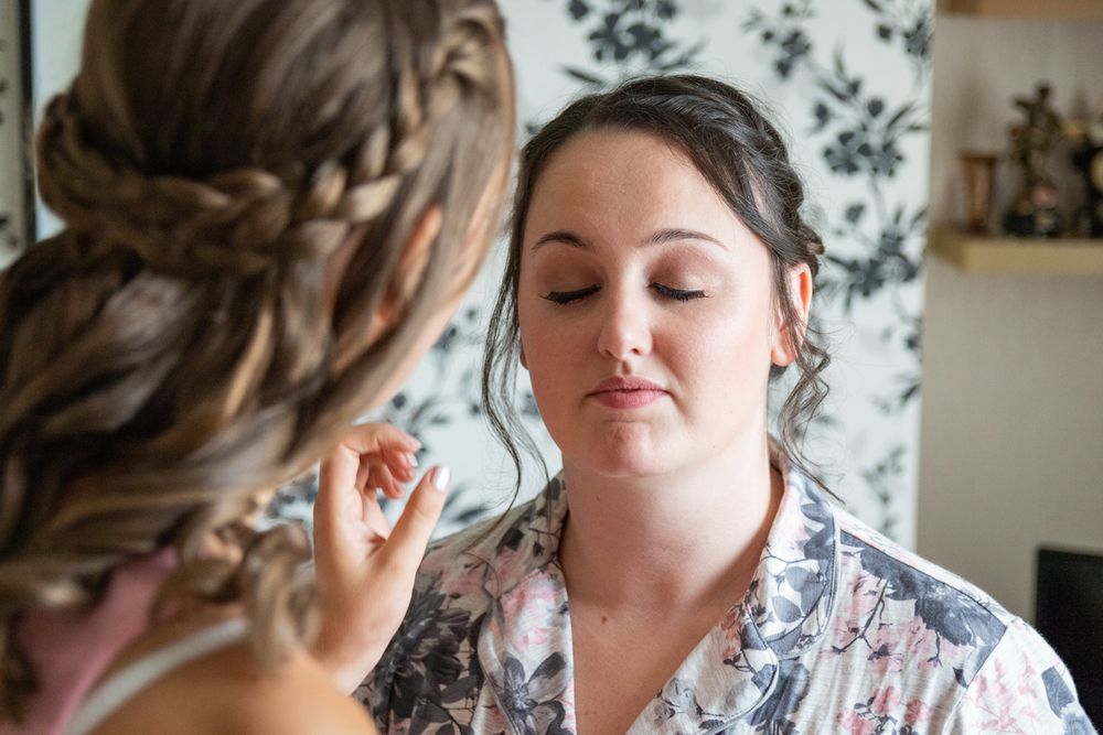 A bridesmaid touching up the brides makeup in the final stages of prep for her wedding. Anglesey Wedding Photography.