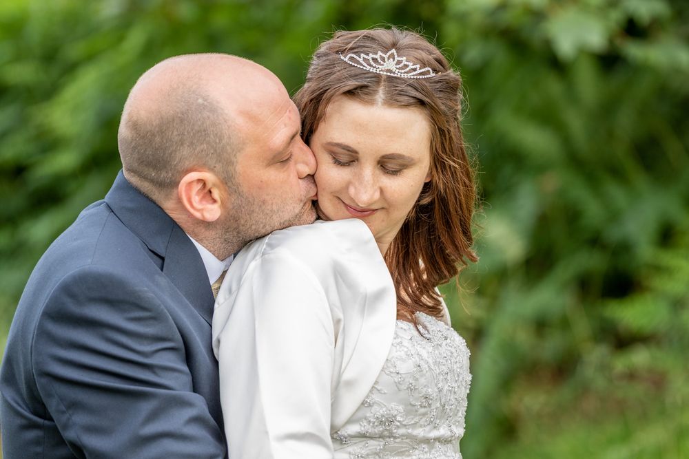 A groom snuggles up behind his groom and kisses her cheek. Bright, colourful wedding photography. Gwynedd Wedding Photographer.