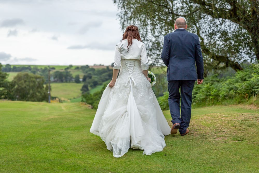 A wedding portrait of a couple holding hands and walking away across the lawns. Bright, colourful wedding photography.