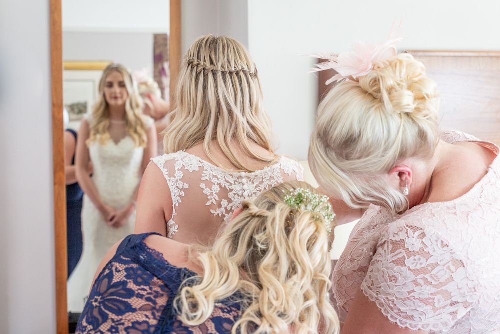 Mother of the bride and maid of honour buttoning up the back of the wedding dress. Bright and airy wedding photography.