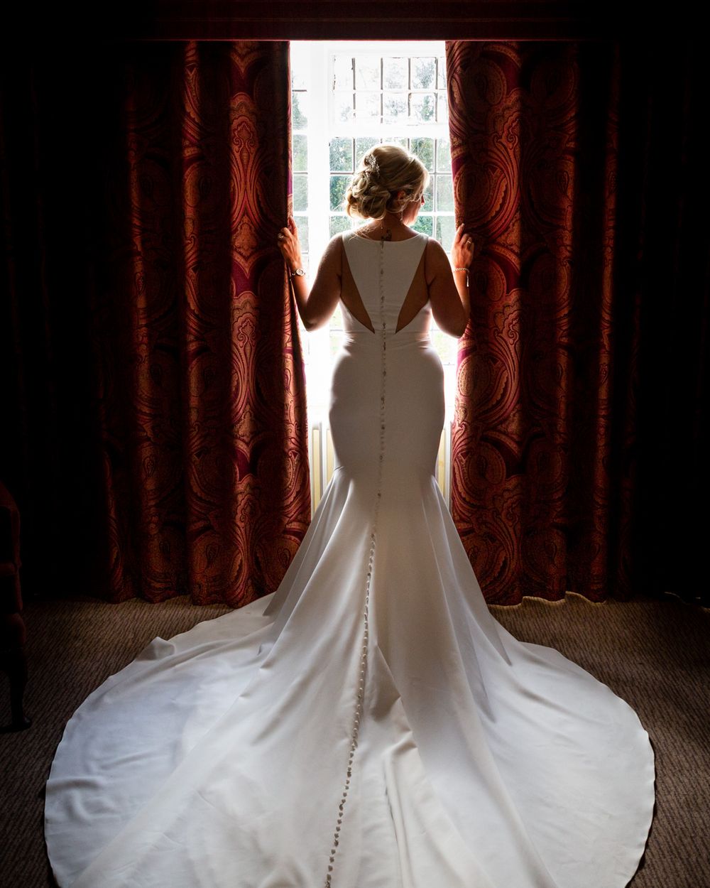 A dramatic semi silhouette portrait of a bride seen from behind as she looks out of a window at MacDonald Craxton Wood.