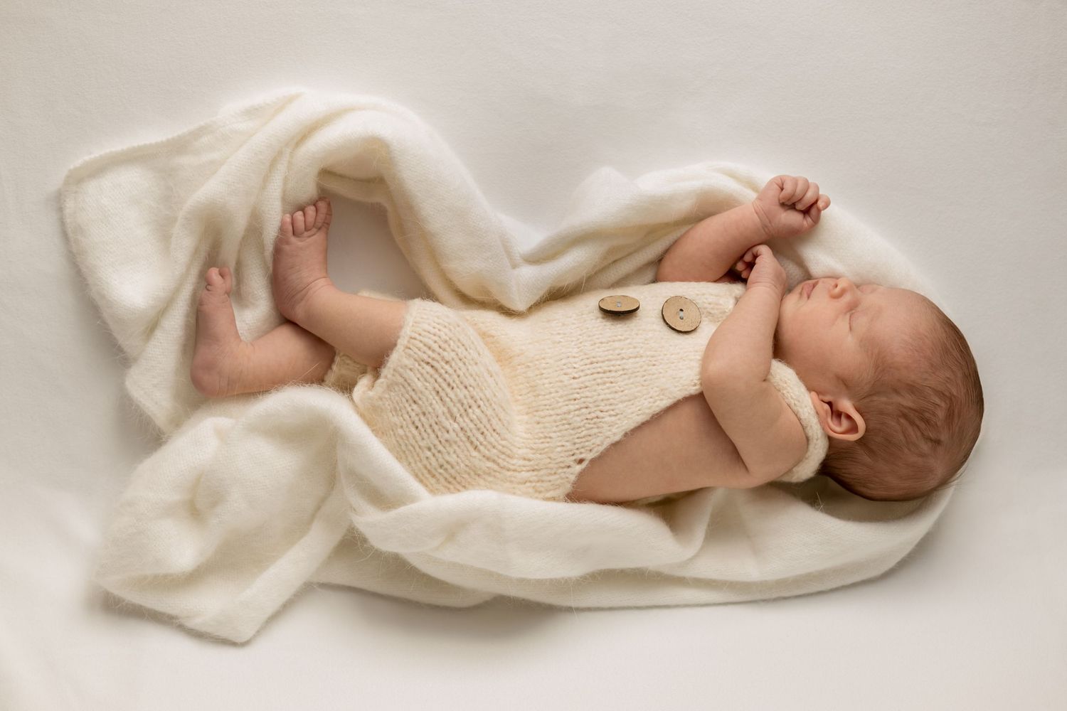 Auckland Natural Newborn photographer. Newborn baby sleeping snuggled up to a white knit wrap. Natural newborn Session. Neutral colours.