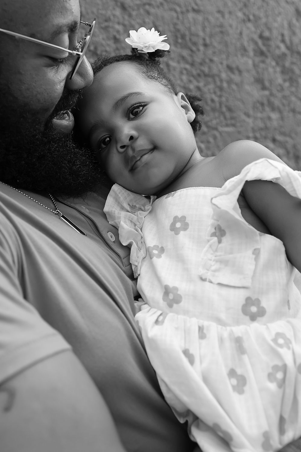 A tender black and white portrait shows an intimate moment between parent and child wearing a floral dress with a white flower.