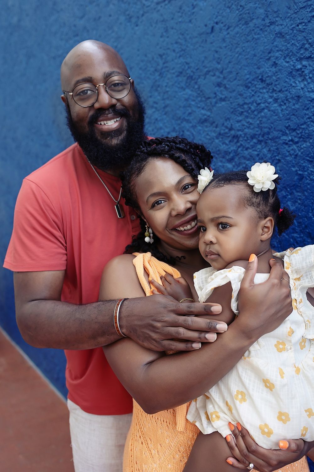A loving family embraces against a bright blue wall background as they smile warmly at the camera at their family portraits in Cancun.