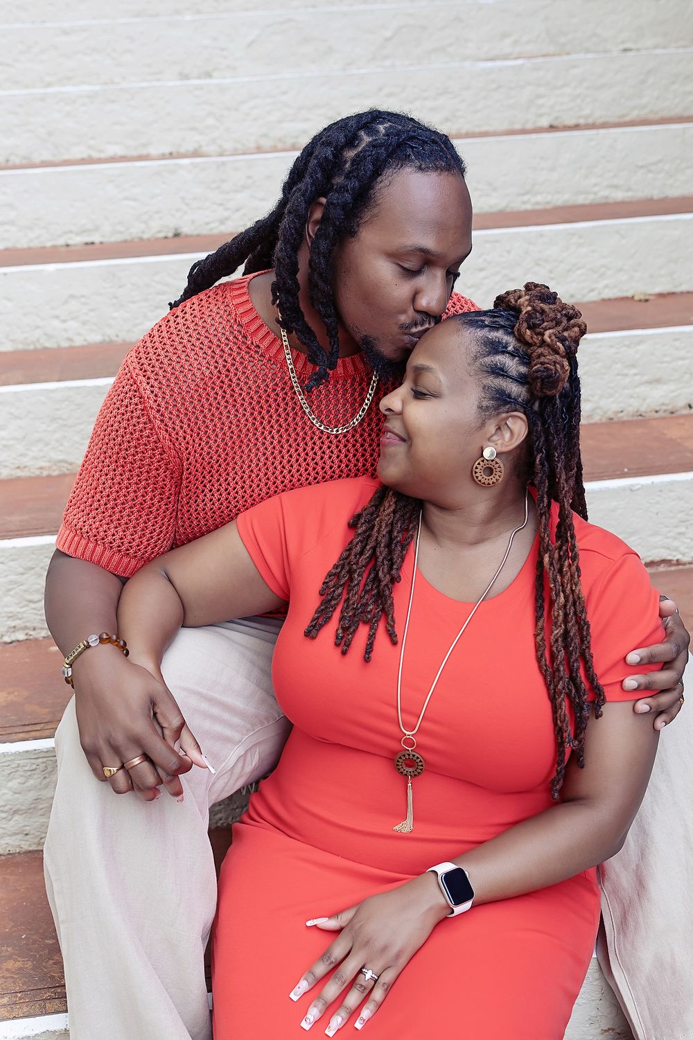 Loving couple on stairs sharing an intimate moment in matching coral outfits with braided hair and jewelry.