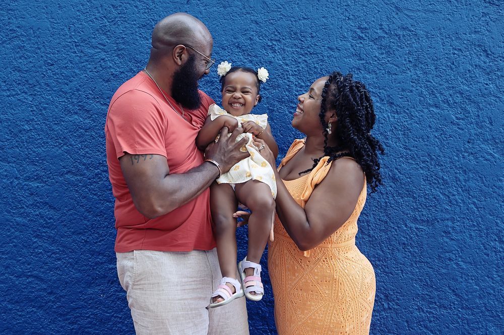 Family shares a joyful moment together against bright blue wall background wearing orange and coral outfits.