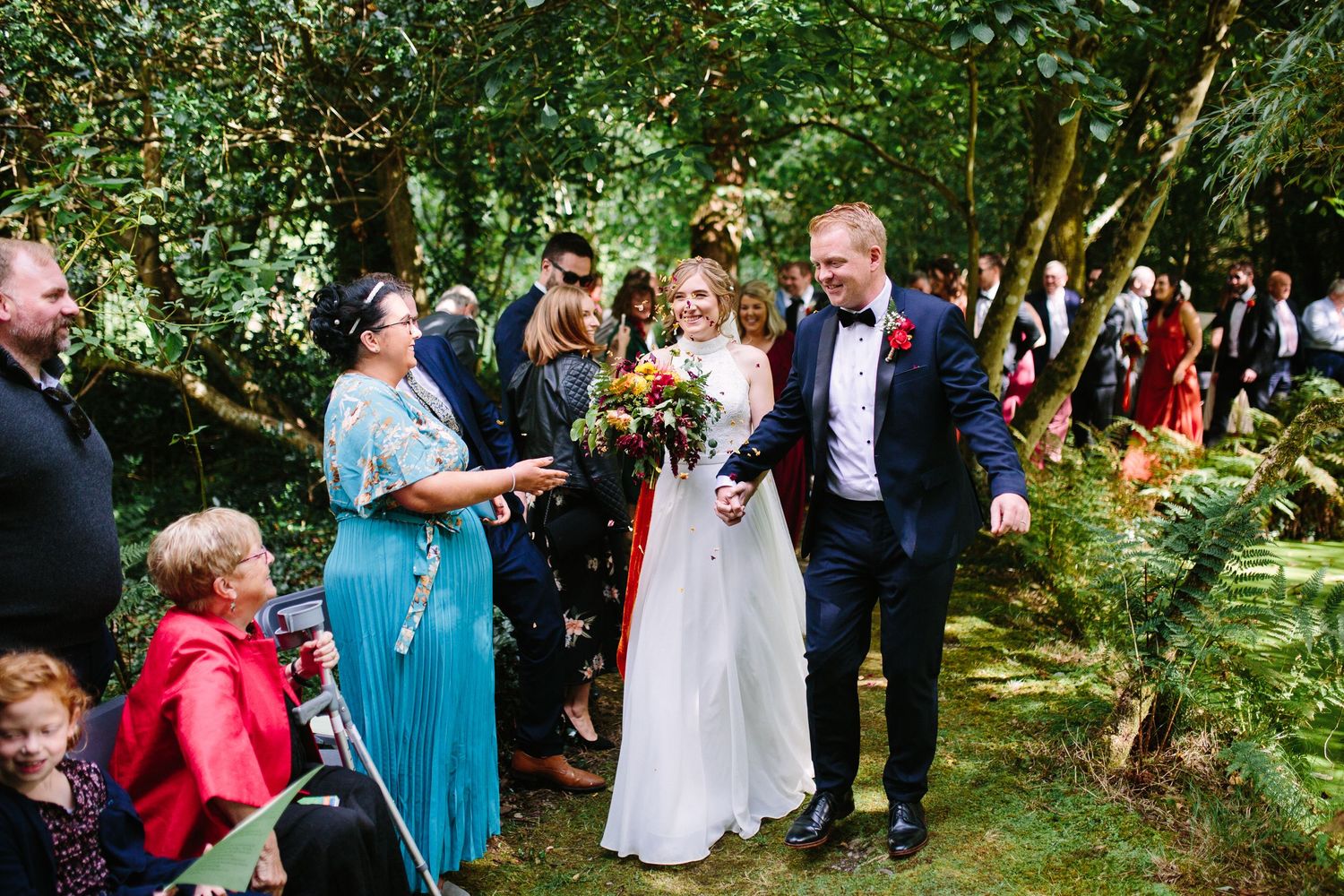 Wedding guests mingle and celebrate in a lush garden setting during an outdoor ceremony reception.