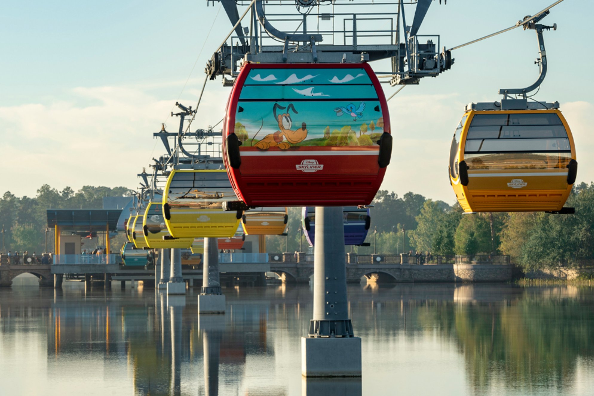 Colorful Disney Skyliner gondolas suspended over a tranquil lake at sunset.