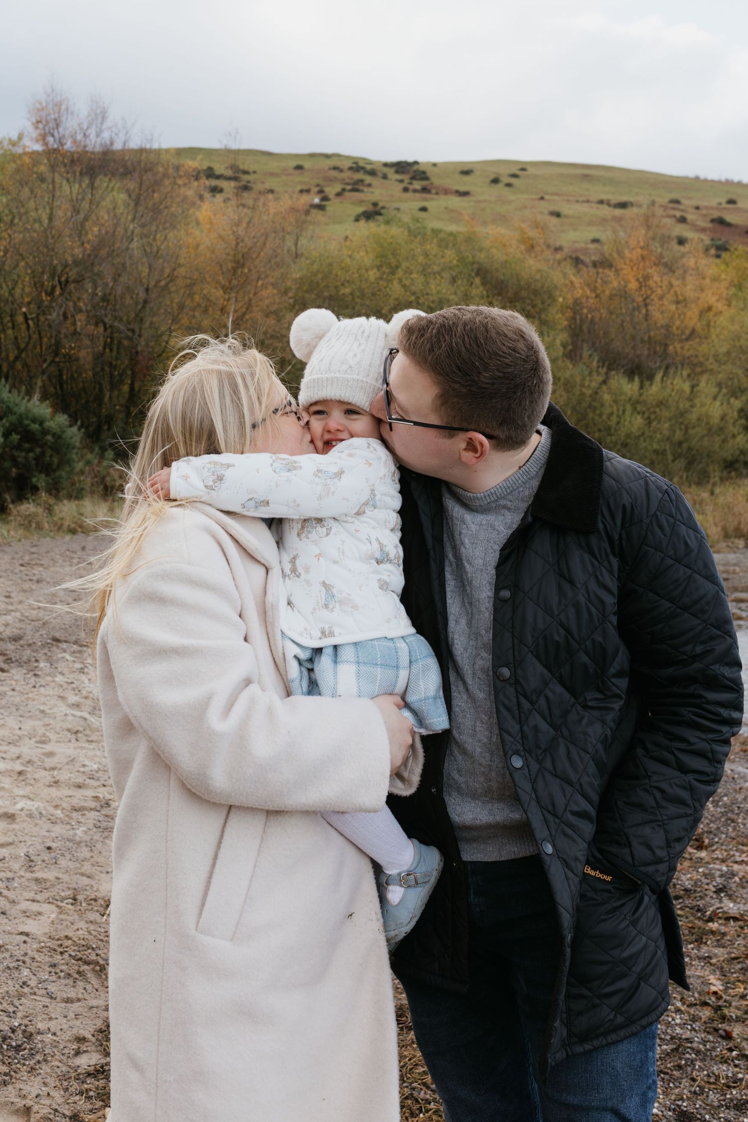 Family sharing a tender moment together on rocky coastal shore during golden hour sunset.