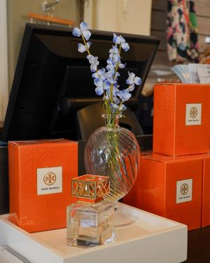 Blue delphinium flowers in glass vase with orange Tory Burch boxes on display.