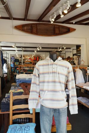 Retail clothing store interior with wooden canoe mounted on wall and striped hoodie display.