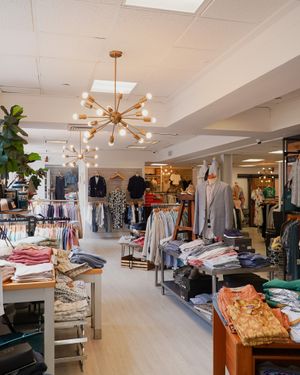 Modern retail store interior with sputnik chandelier and organized clothing displays.