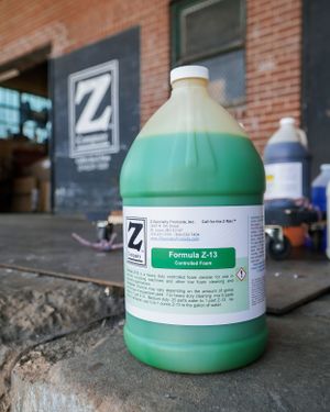 A large green gallon jug of Formula Z-15 cleaning solution sits on a brick ledge with a company logo in the background.