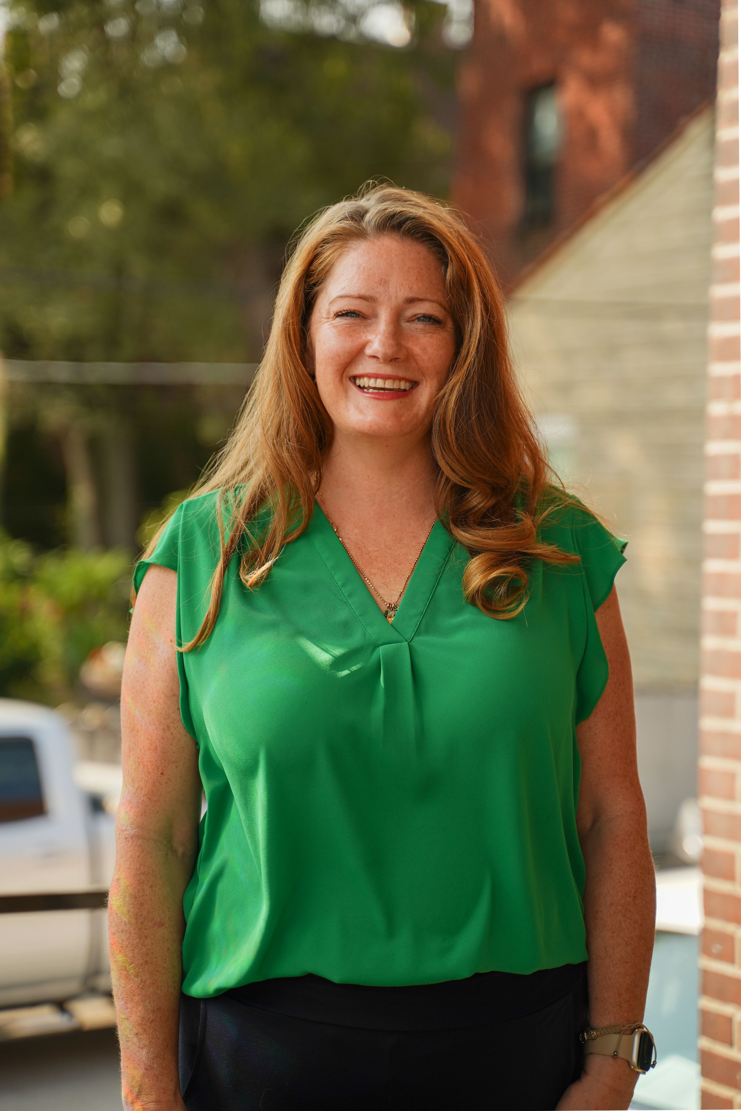 A professional woman in a green blouse poses outdoors against a brick building backdrop.