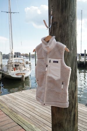 White fleece vest hanging on a wooden post at a marina with sailboats in the background.
