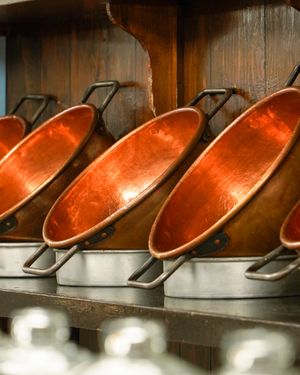 Row of copper serving pans arranged on wooden shelf display.