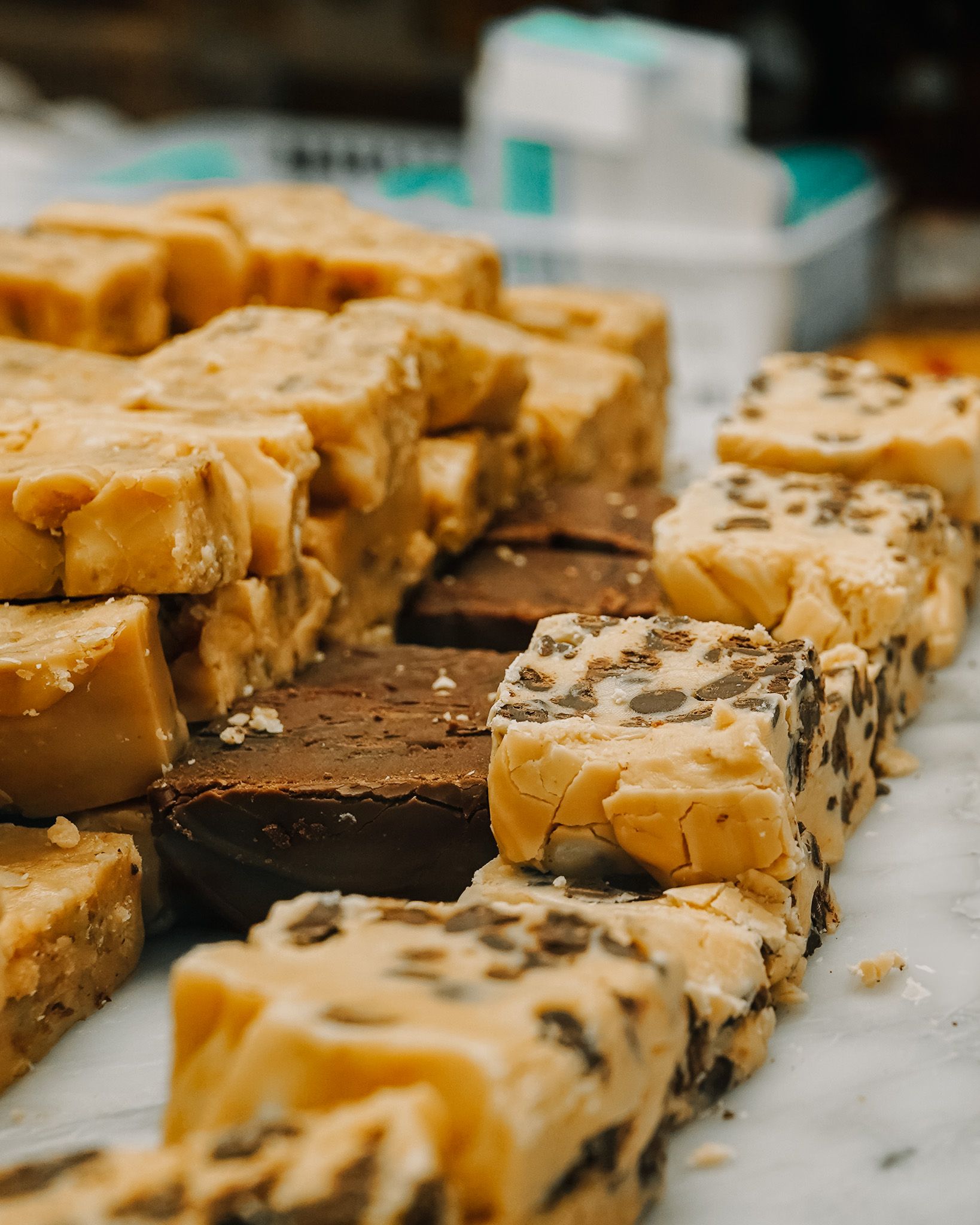 Rows of homemade fudge slices with various toppings on marble surface.