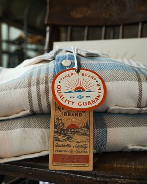 Stack of plaid blankets with vintage quality guarantee tag displayed on wooden surface.