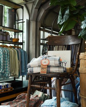 Retail display of folded plaid textiles on antique wooden chair in clothing store.