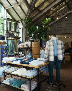 Retail clothing display with plaid shirts and casual wear arranged on wooden shelves under exposed beam ceiling.