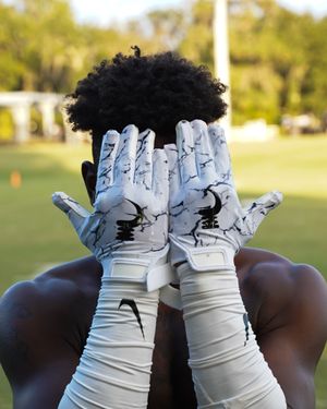 Athletic gloves with white and light blue marble pattern design held up against outdoor field.