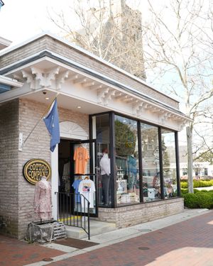 Brick storefront with large windows displaying clothing and a navy blue flag.
