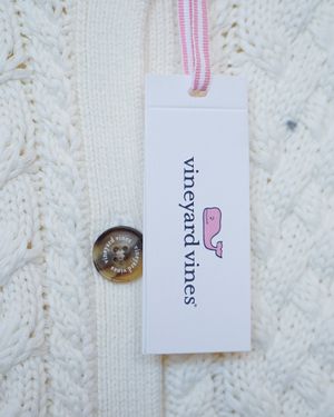 White clothing tag with pink whale logo against knit sweater texture.