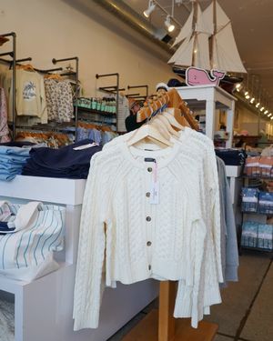 White cable knit cardigan displayed on rack in retail clothing store with nautical decor.
