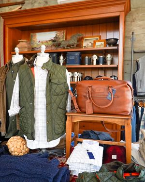 Green quilted vest and leather duffle bag displayed on wooden shelf with casual menswear.