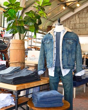 Retail display of denim jacket, jeans, and accessories with a large potted plant in the corner.